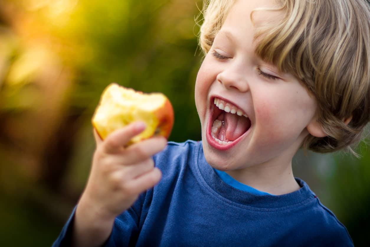 Small child smiling and laughing while biting into an apple
